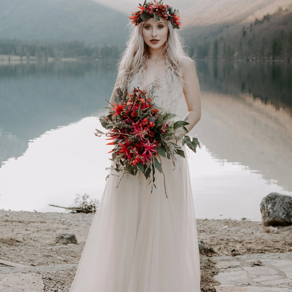 Bride wearing the Champagne Lace and Tulle Wedding dress 1205, holding a red  wild flower bouquet beside a mountain lake.