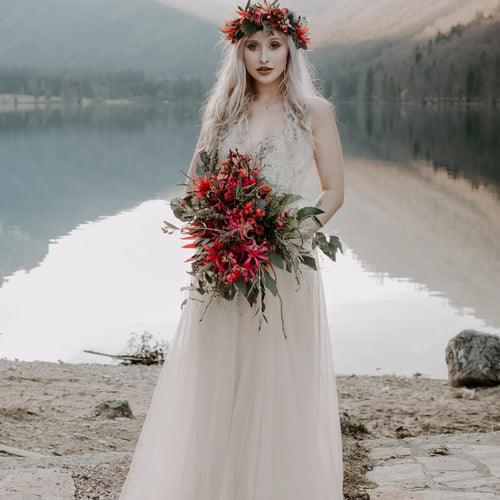 Bride wearing the Champagne Lace and Tulle Wedding dress 1205, holding a red  wild flower bouquet beside a mountain lake.