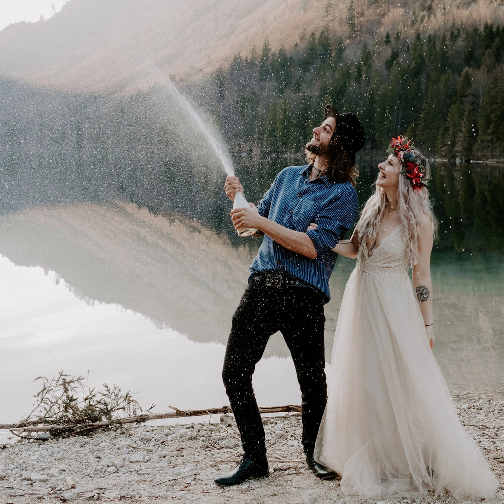 Bride wearing the Champage Lace and Tulle Wedding Dress as her partner sprays champagne beside a mountain lake.