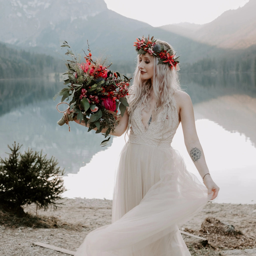 Bride wearing the Champagne Lace and Tulle Wedding dress, holding a red wildflower bouquet as the flowing skirt moves besides a mountain lake.