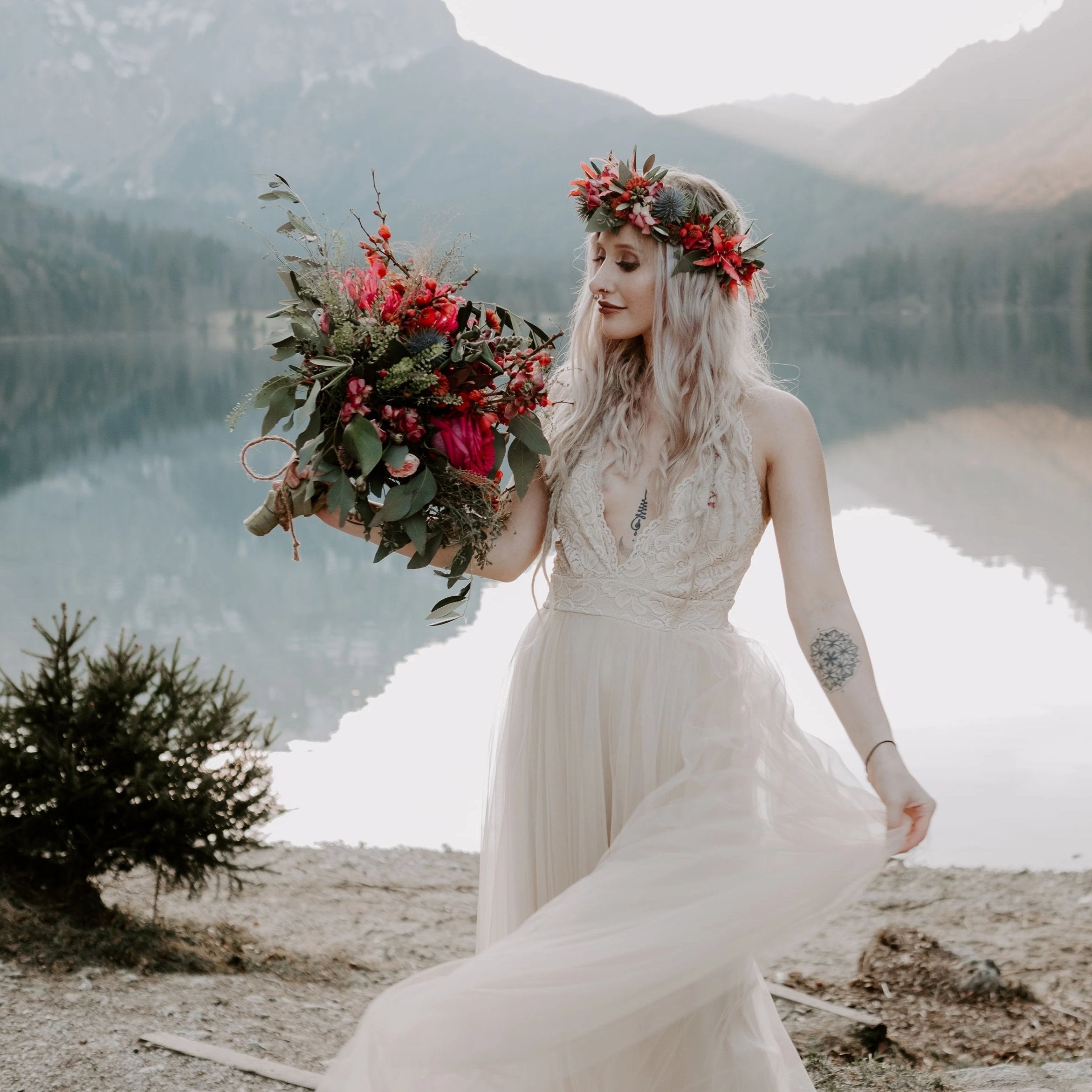 Bride wearing the Champagne Lace and Tulle Wedding dress, holding a red wildflower bouquet as the flowing skirt moves besides a mountain lake.