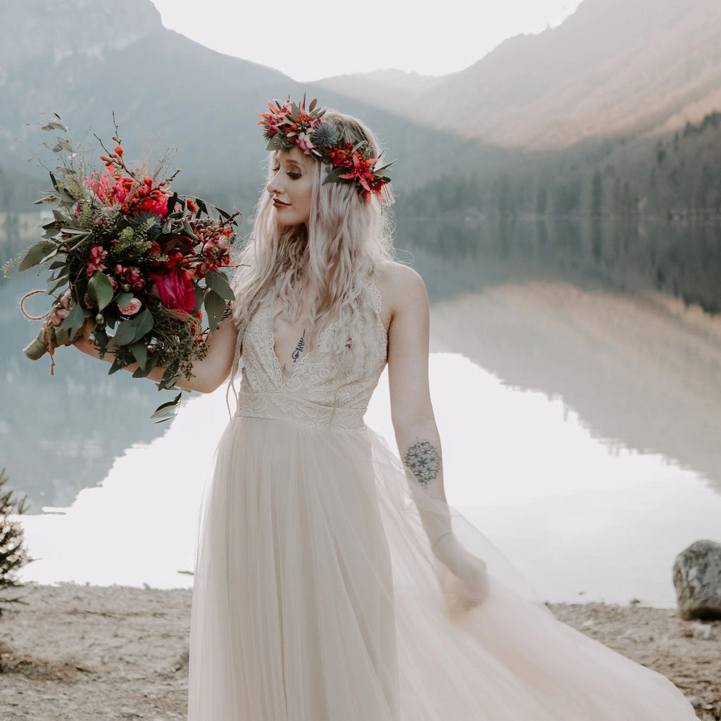 Bride wearing the Champagne Lace and Tulle Wedding Dress 1205, lifting the flowing tulle skirt beside a mountain lake.