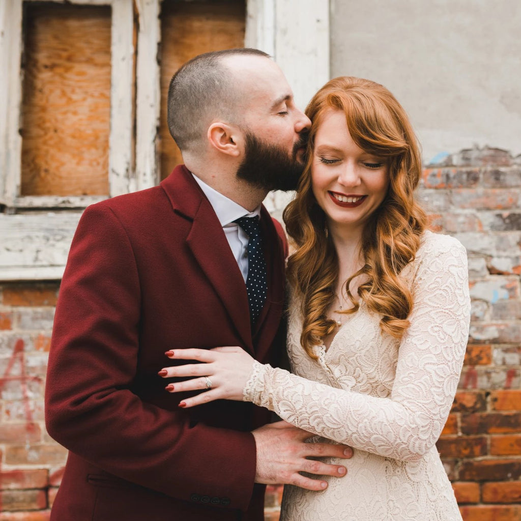 Smiling bride in a champagne lace wrap wedding gown with long sleeves beside with groom outdoors