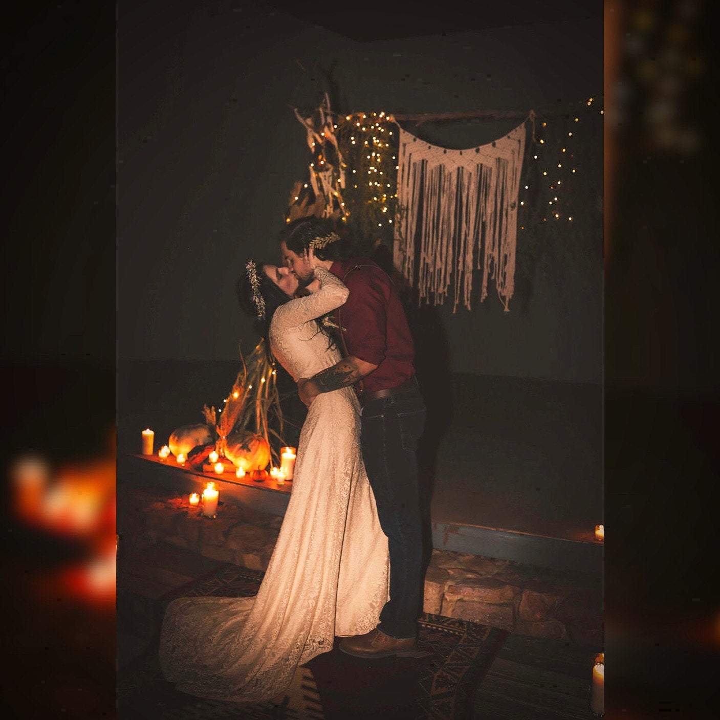 Bride in a champagne lace wrap wedding gown with long sleeves embracing groom at a candlelit venue.
