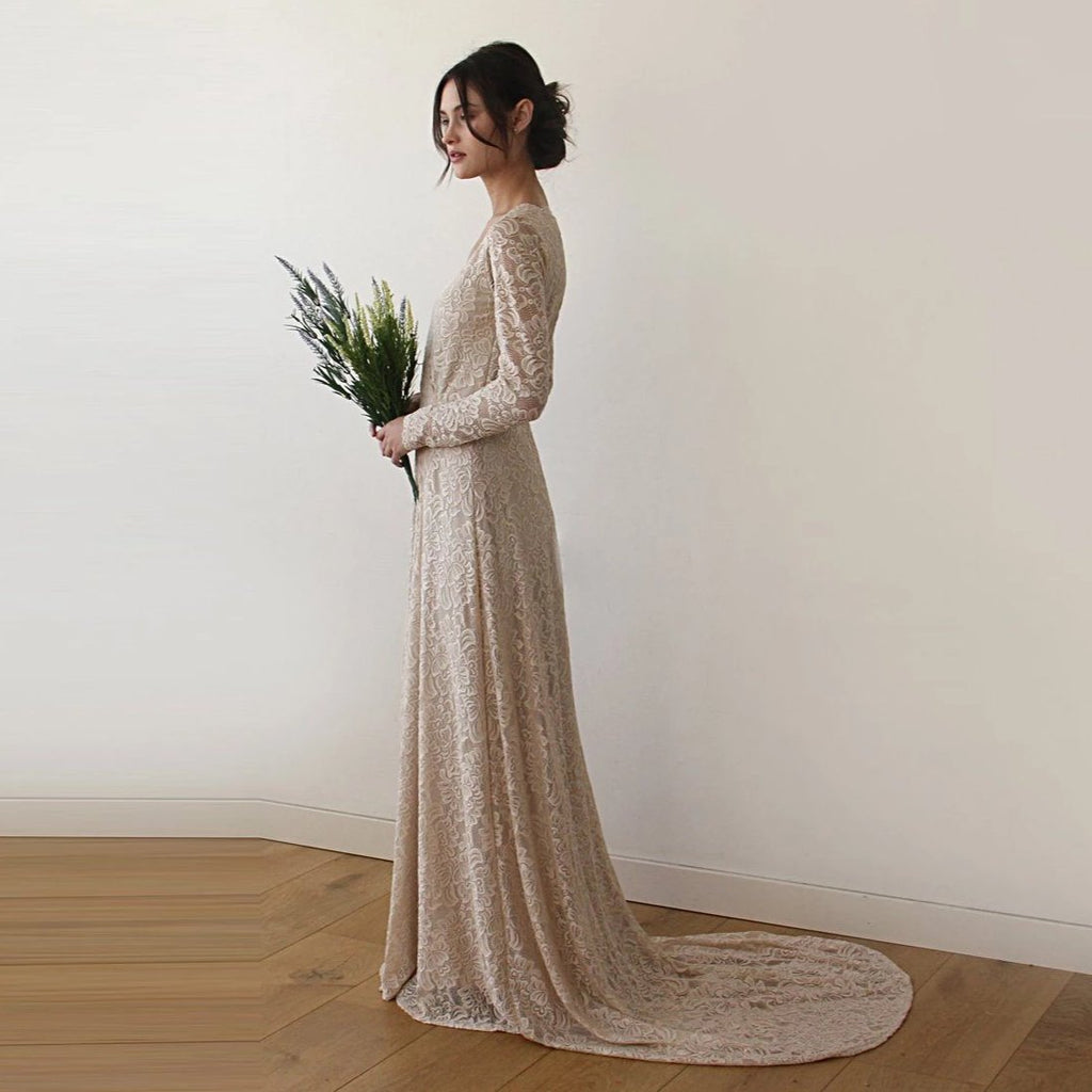 Bride wearing a champagne lace wrap wedding gown with long sleeves and train holding flowers.