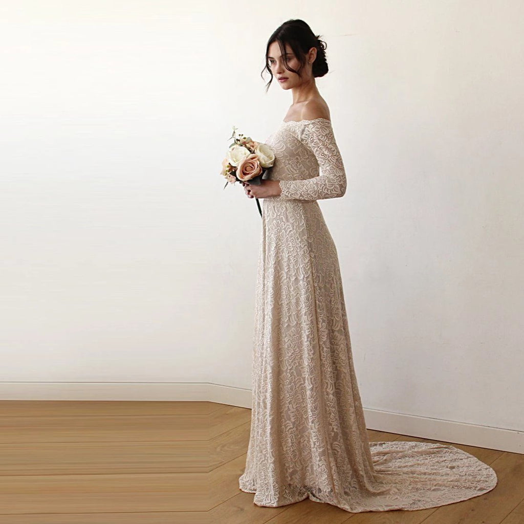 Left-side view of model wearing a champagne off-shoulder lace wedding gown with long sleeves, fitted silhouette, bouquet, and floor-length train.