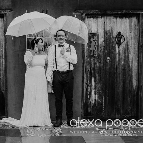 Bride and groom standing under umbrellas in a black-and-white wedding portrait, bride wearing a champagne off-shoulder lace wedding gown with train.