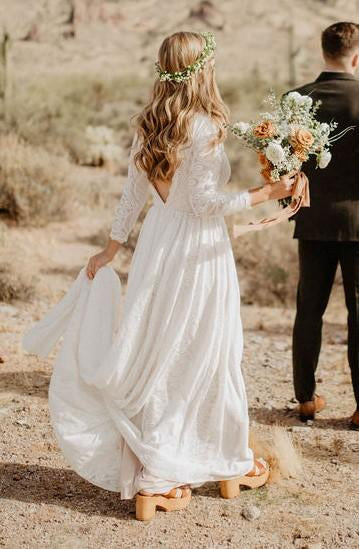 Rear view of bride with peach bouquet in a Ivory open back lace wedding gown showing deep V open back detail, long lace sleeves and flowing floor-length skirt with train — desert elopement setting —Curated by  Douceur de Vivre Parisn