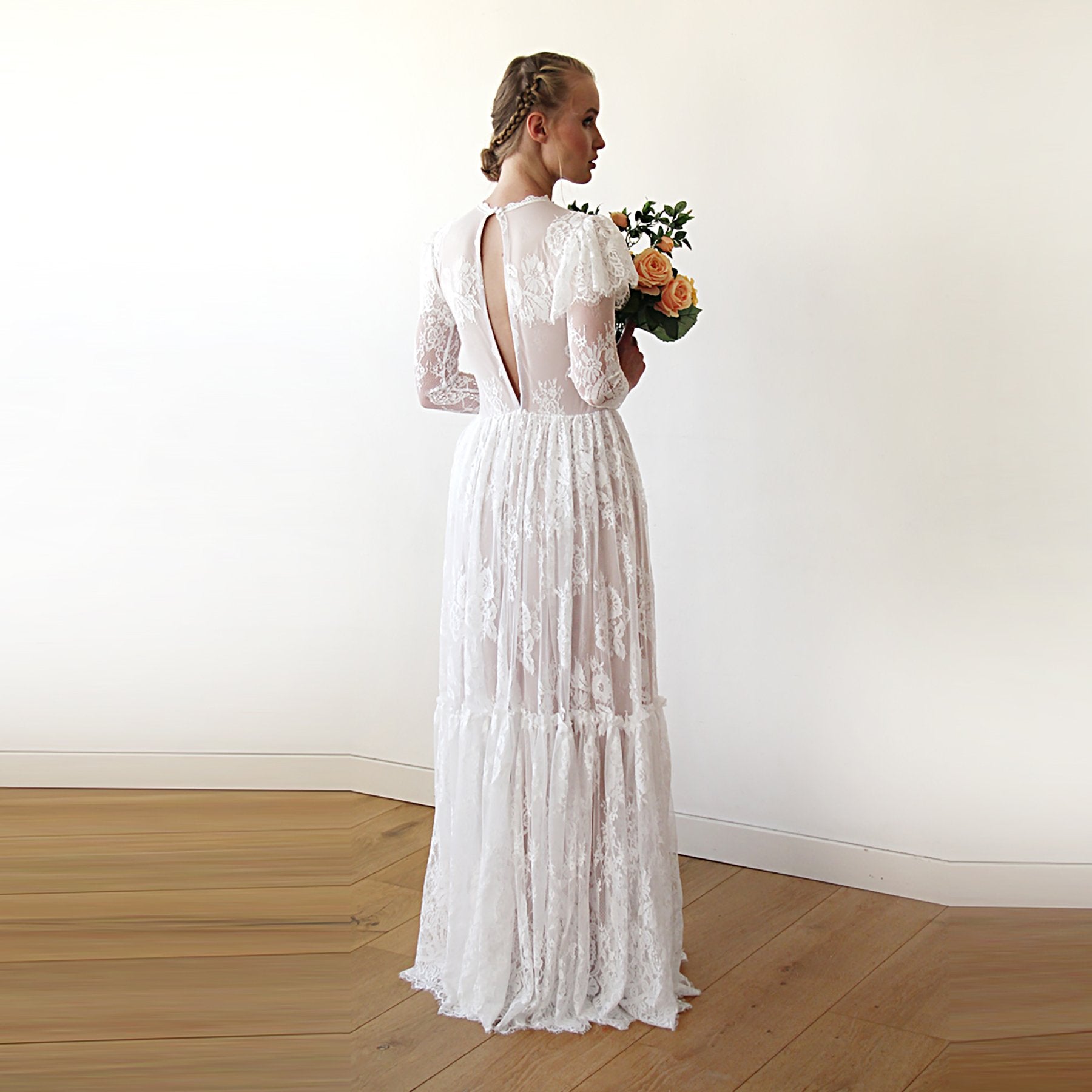 Back view of model with a bouquet, wearing a champagne woodland vintage lace wedding gown with open keyhole back, flutter sleeves, sheer lace sleeves, and floor-length tiered skirt.