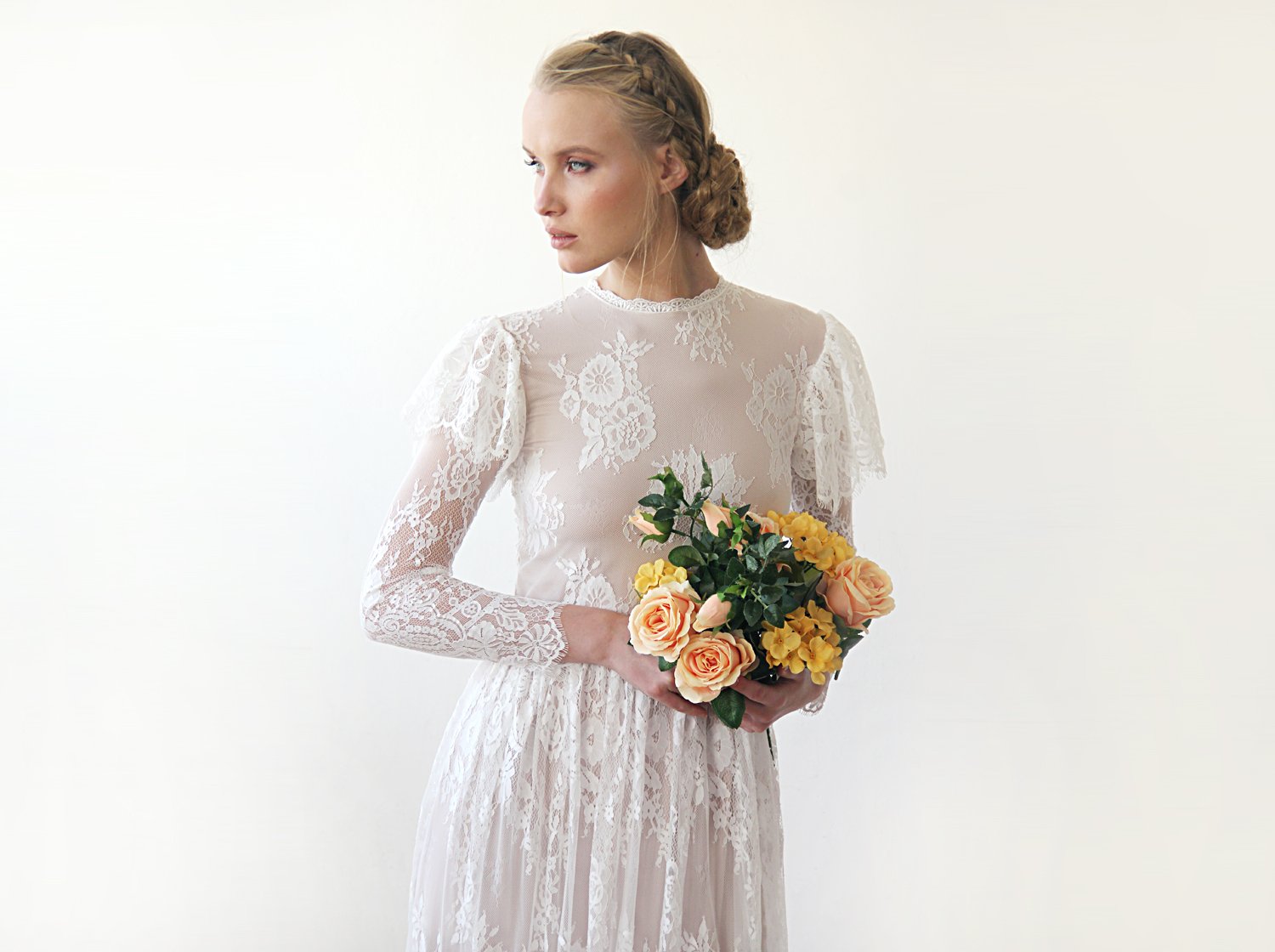 Close-up front view of model with a rose bouquet wearing a champagne woodland vintage lace wedding gown with high neckline, sheer long lace sleeves, flutter sleeve overlay, and bridal bouquet.