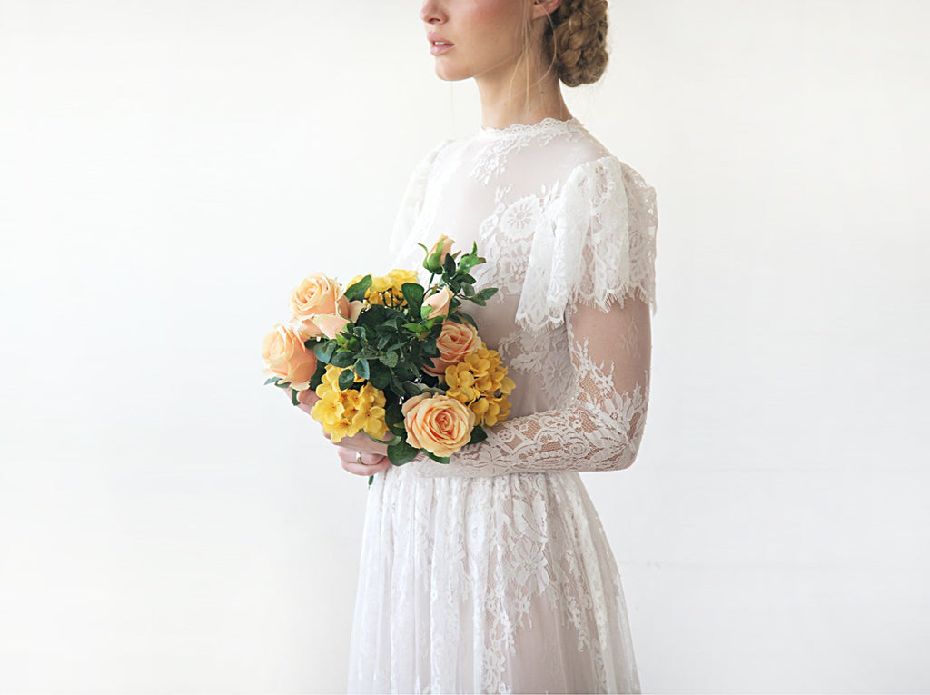 Cropped side view of model  with a bridal bouquet wearing an ivory woodland vintage lace wedding gown with high neckline, flutter sleeve overlay, sheer long lace sleeves, and bridal bouquet.