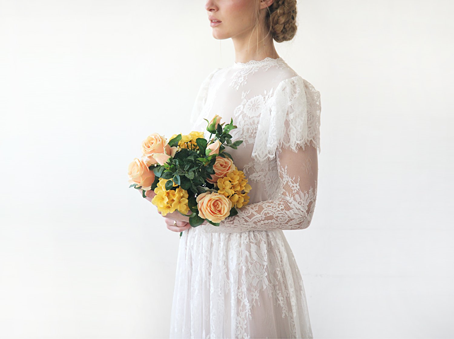 Cropped side view of model  with a bridal bouquet wearing an ivory woodland vintage lace wedding gown with high neckline, flutter sleeve overlay, sheer long lace sleeves, and bridal bouquet.