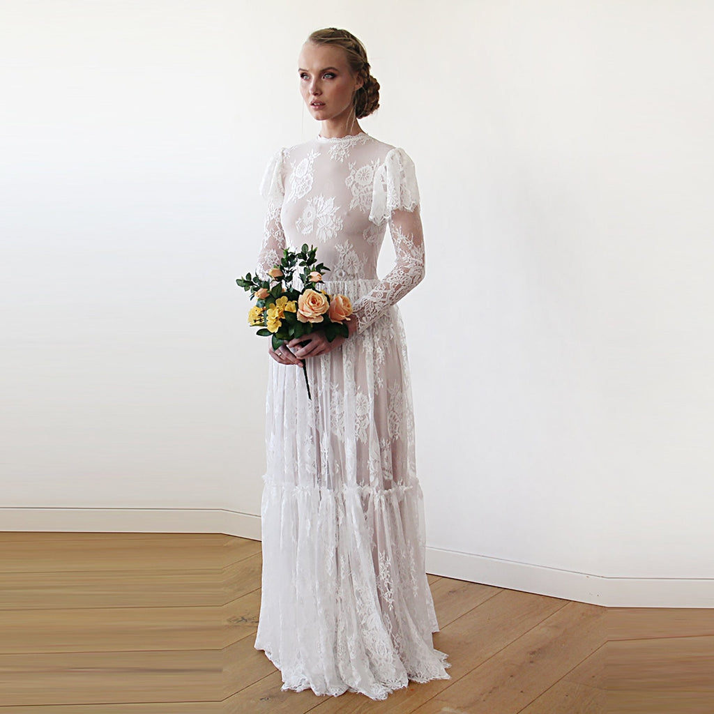 Front view of model wearing a champagne woodland vintage lace wedding gown with high neckline, flutter sleeves, sheer lace sleeves, bouquet, and floor-length tiered skirt.