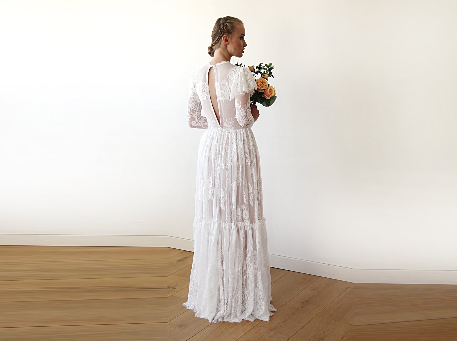 Full-length back view of model wearing an ivory woodland vintage lace wedding gown with open keyhole back, flutter sleeve overlay, sheer long lace sleeves, tiered skirt, and bridal bouquet.