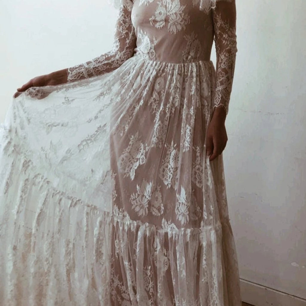 Close-up detail of an ivory woodland vintage lace wedding gown showing floral lace bodice, sheer long lace sleeve, soft lining, and tiered lace skirt.