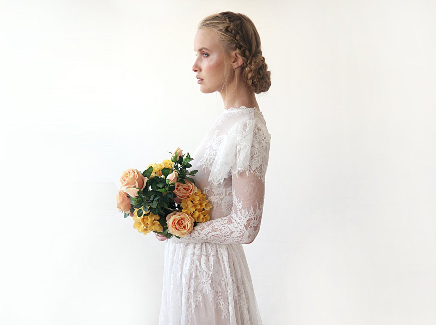 Side view of model with a bridal bouquet wearing an ivory woodland vintage lace wedding gown with high neckline, sheer long lace sleeves, flutter sleeve overlay, and bridal bouquet.